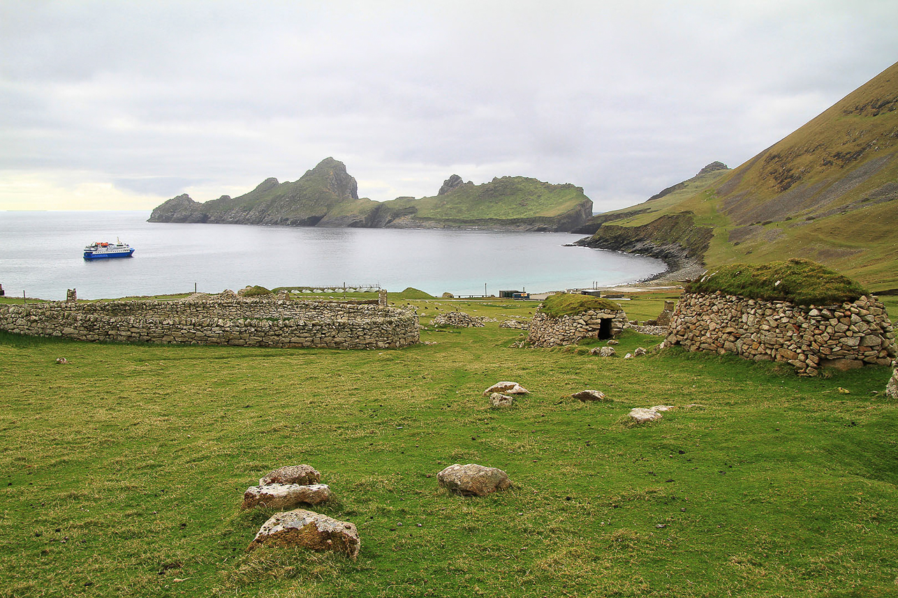 View of St Kilda and Village Bay. Graveyard (inside the circular stone wall) and storage houses in front.